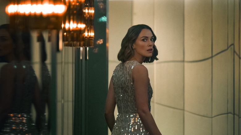Lo in a sparkly gown walking down a hallway and looking over her shoulder in the Woman in Cabin 10