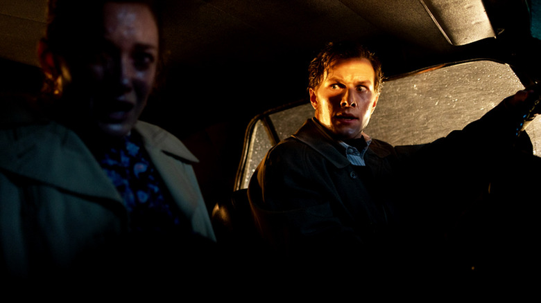Ed Warren in the driver's seat of a car, looking frantically at a female passenger in The Conjuring: Last Rites