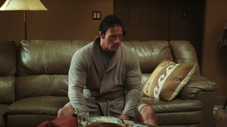 Dwayne Johnson as Mark Kerr sitting in a robe on the couch in The Smashing Machine