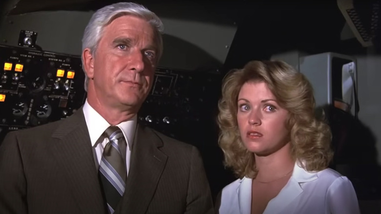 Leslie Nielsen's Dr. Rumack and Julie Hagerty's Elaine Dickinson standing next to a control panel in Airplane!