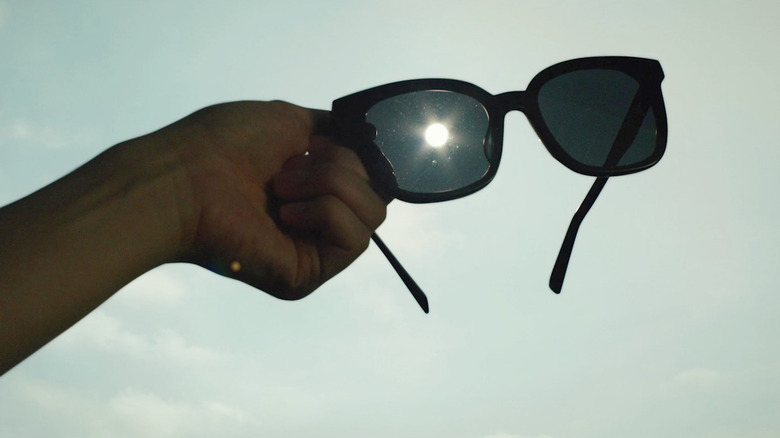 A hand holding a pair of sunglasses (with the sun in the middle) in Parasite