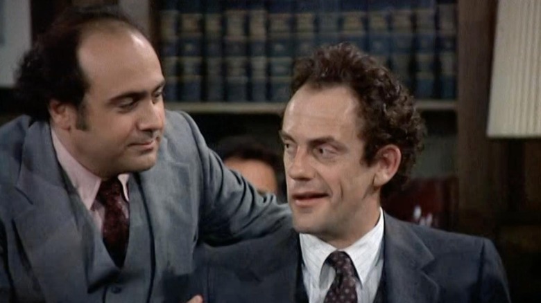 Louie De Palma (Danny DeVito) stands next to Reverend Jim Ignatowski (Christopher Lloyd) in "Taxi"