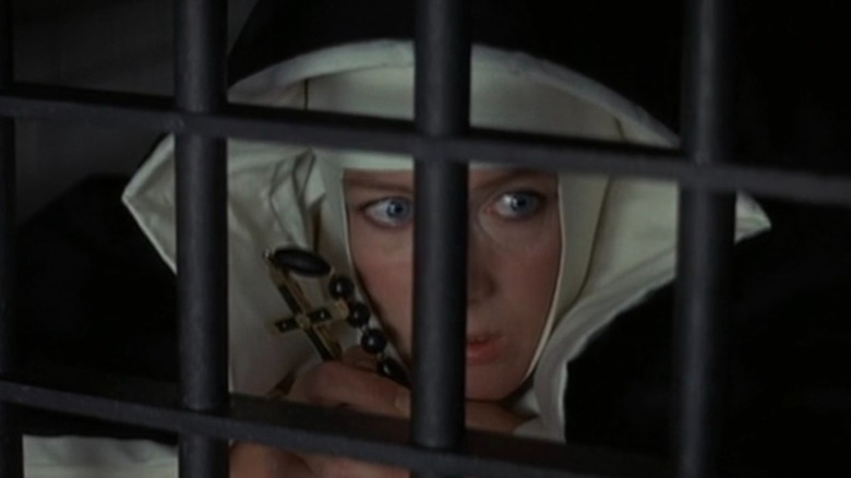 Sister Jeanne holding a crucifix behind bars in The Devils