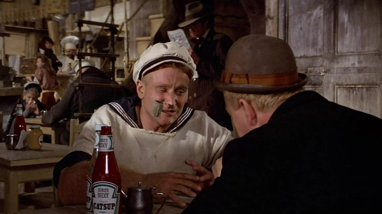Popeye with a tube sitting on a wimpy table in Popeye