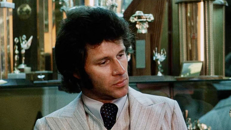 H.B. Halicki as Maindrian Pace wearing a pin-striped suit in an office filled with trophies in Gone in 60 Seconds