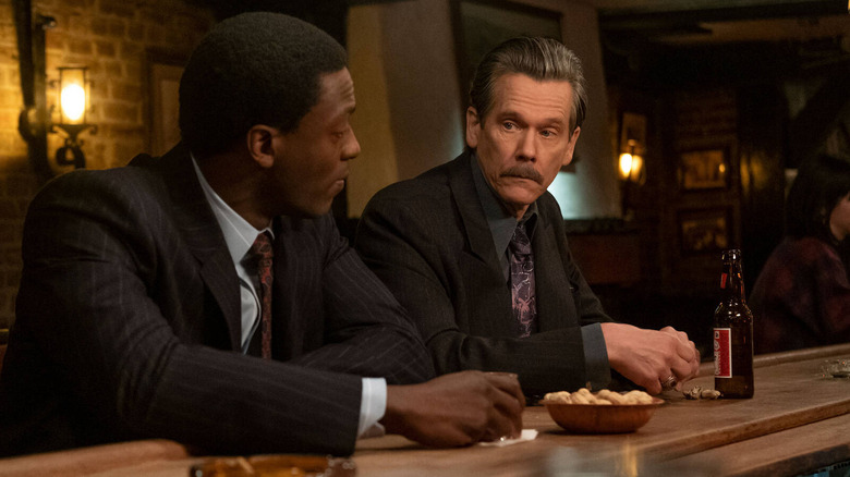 Aldis Hodge and Kevin Bacon wearing suits and sitting side by side at a bar in City on a Hill