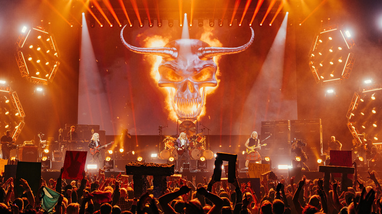Spinal Tap plays with a fiery background on a massive orange-lit stage in a reunion concert for Spinal Tap 2