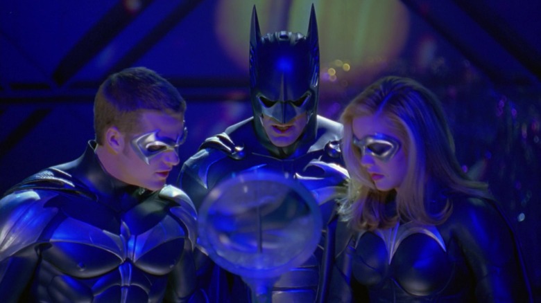 Robin, Batman, and Batgirl gathered around a large magnifying lens in Batman & Robin