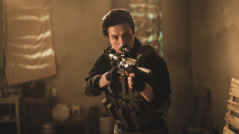 Jeong Jin-man (Lee Dong-wook) aims an assault rifle in a dark room in A Shop for Killers