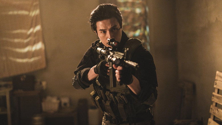 Jeong Jin-man (Lee Dong-wook) aims an assault rifle in a dark room in A Shop for Killers