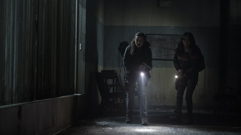 Dina and Ellie making their way through the dark with flashlights on The Last of Us