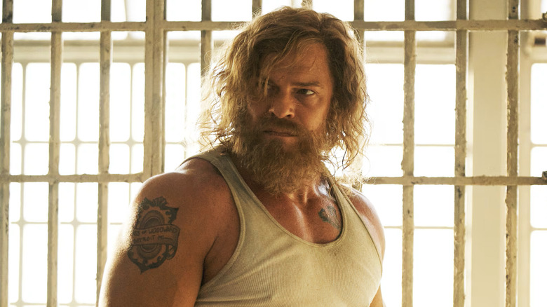 A bearded John Miller (Alan Ritchson) looking around angrily in prison in Motor City