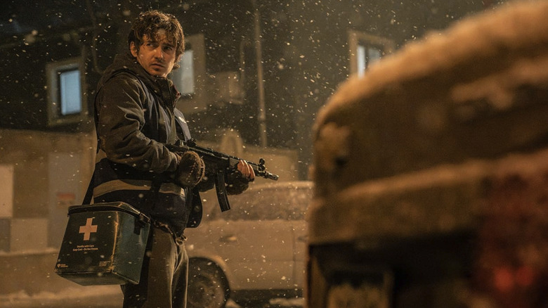 Bryan carrying a gun and a medical bag, standing outside in the snow, in Resident Evil