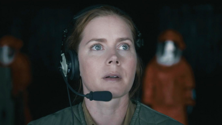 Amy Adams' Louise Banks stands with a headset on in front of people in hazmat suits in Arrival