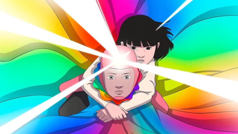 Juliano Valdi as Arco wearing a rainbow cape with rays emanating from his forehead and Romy Fay as Iris clinging to his back in Arco