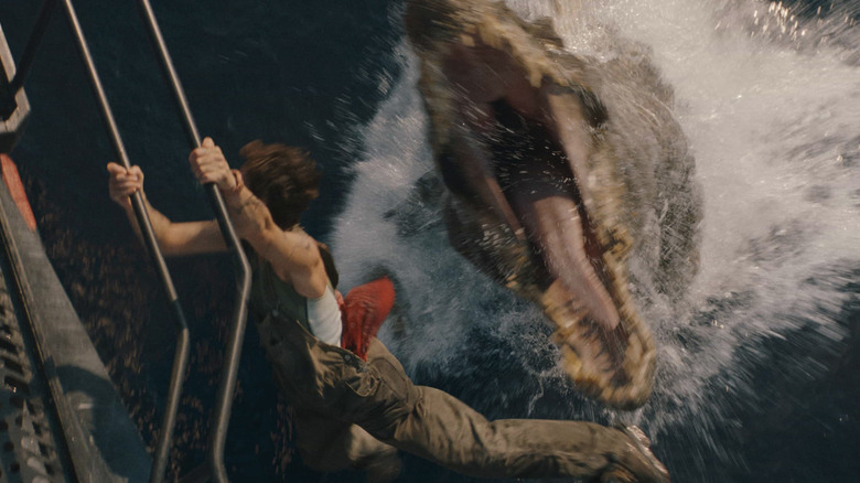 A dinosaur opens its mouth and leaps out of the water, trying to eat a person hanging from a boat railing in Jurassic World Rebirth