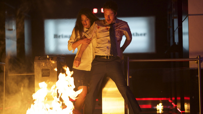 John Gallagher Jr. as Mike and Adria Arjona as Leandra dodging a fire in The Belko Experiment