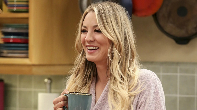 Penny holds a cup of coffee and laughs at The Big Bang Theory