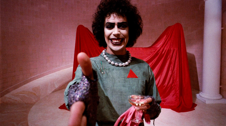 Dr. Frank N. Furter (Tim Curry) extends his hand for a handshake in The Rocky Horror Picture Show