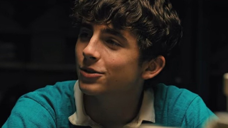 A close up of Timothee Chalamet as Daniel smirking with his head cocked to the side while sitting down in Hot Summer Nights