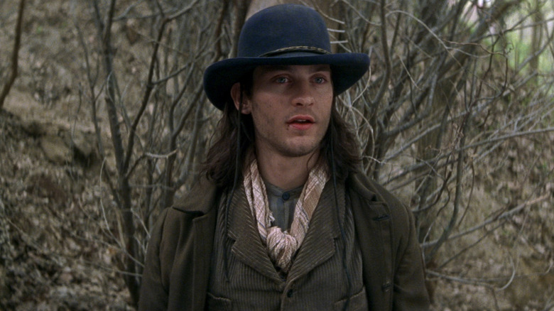 Tobey Maguire as Jake Roedel wearing a hat while standing in a forest in Ride with the Devil