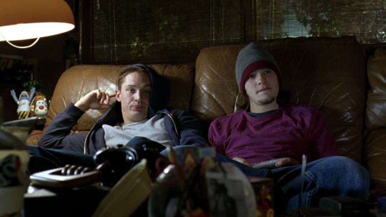 Tom Hardy's Tom sits on a couch alongside Charlie Cox's Theo as they watch TV in Dot the I