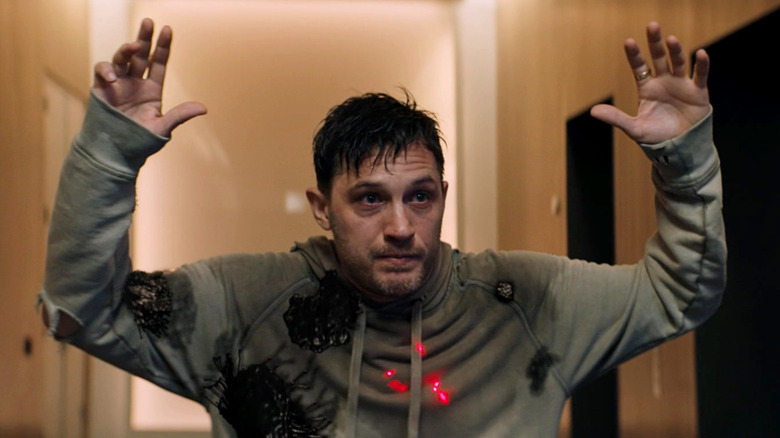 Tom Hardy as Eddie Brock AKA Venom, looking sweaty and holding his hands over his head
