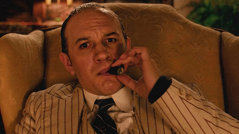 Tom Hardy fumando un cigarro y mirando la lente de la cámara como Al Capone en Capone