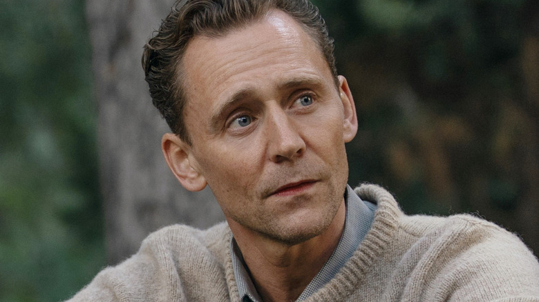 Tom Hiddleston sitting in a forest wearing a sweater as Sir Edmund Hillary in Tenzing