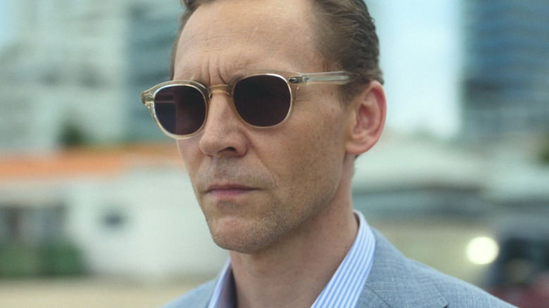 Tom Hiddleston's Jonathan Pine is seen in closeup wearing shades while standing outside in The Night Manager
