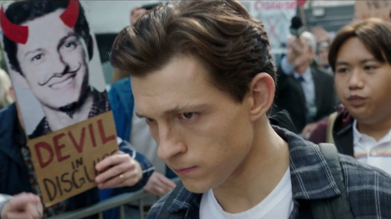 Tom Holland como Peter Parker passando por uma placa de protesto chamando-o de diabo disfarçado em Homem-Aranha: No Way Home