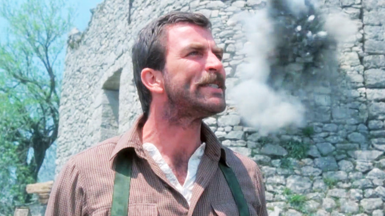 Tom Selleck's Patrick O'Malley looks up as a wall explodes behind him in High Road to China