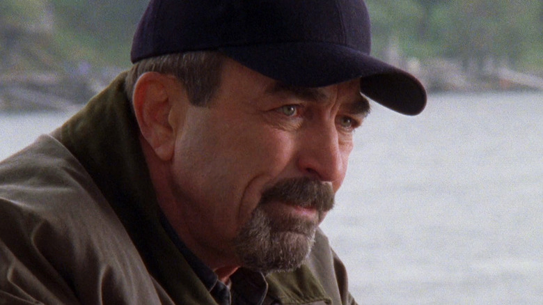 Tom Selleck's Jesse Stone looks off into the distance as he sits by the ocean in Jesse Stone Innocents Lost
