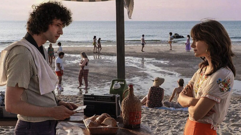 Tony and Nancy standing at the beach while people mill around behind them in Tony