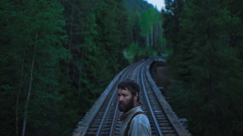 Robert Grainier stands on a railroad bridge in Train Dreams