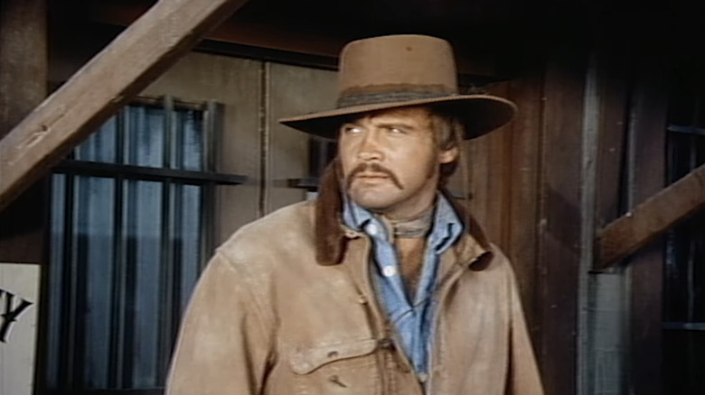 Lee Majors' Roy Tate stands on a porch looking off to his right in The Men from Shiloh