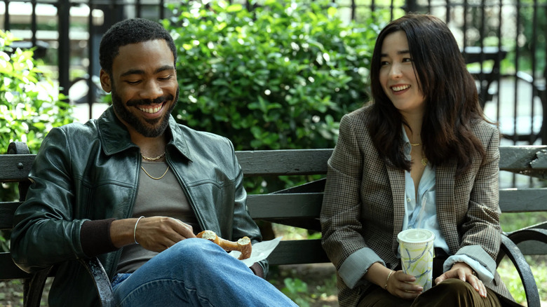 Donald Glover and Maya Erskine as Mr. and Mrs. Smith, laughing together on a park bench on Mr. and Mrs. Smith