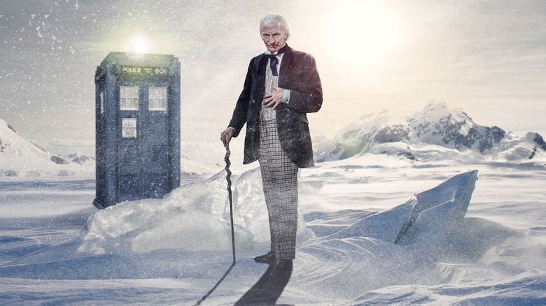 William Hartnell as the First Doctor standing in the snow next to the TARDIS from Doctor Who