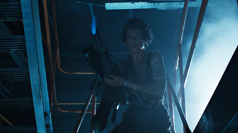 Sigourney Weaver's Ripley looks worried as she carries a flamethrower down some steps in Aliens