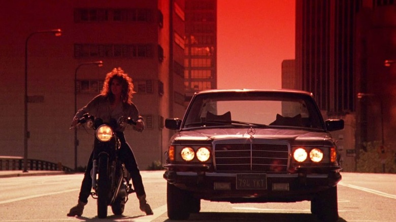 Reggie Belmont (Catherine Mary Stewart) rides a motorcycle next to an empty car in Night of the Comet