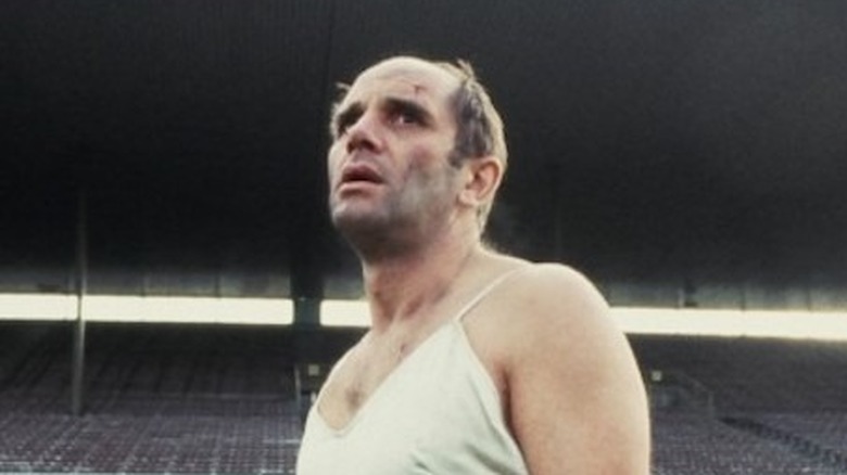 Man in a nightgown standing in empty sports stadium in The Quiet Earth