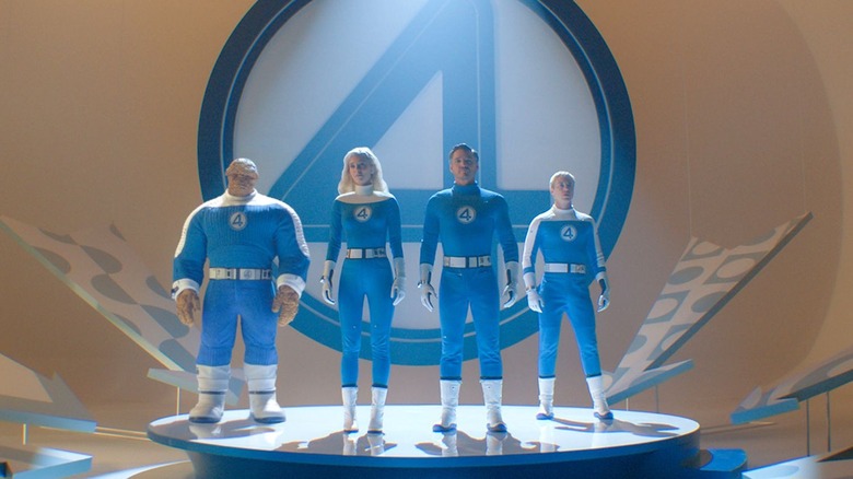 The Thing, Sue Storm, Reed Richards, and Johnny Storm pose heroically on stage in front of their Fantastic Four logo in The Fantastic Four: First Steps