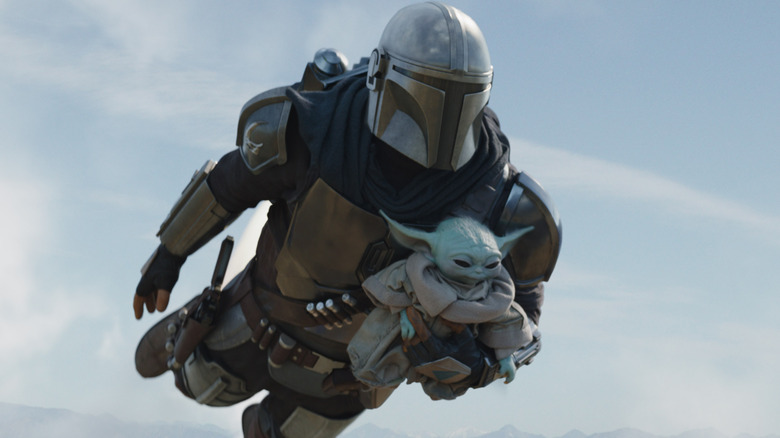 The Mandalorian and Grogu fly through the air with Din Djarin's jetpack in The Mandalorian