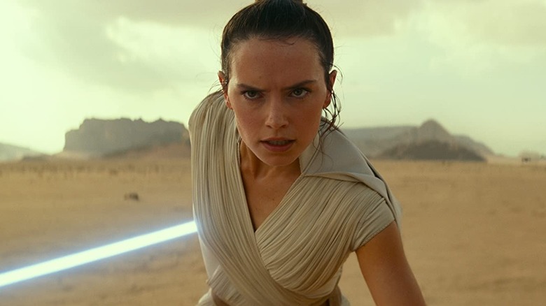 Daisy Ridley as Rey with her lightsaber to her side in the desert of Pasaana in Star Wars: The Rise of Skywalker