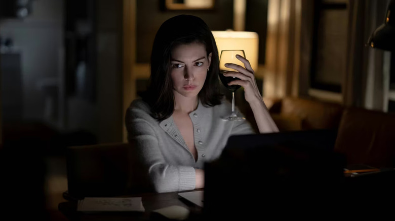 Verity writing at her laptop and holding a wine glass in Verity