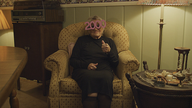An elderly woman sits in a chair in V/H/S/99