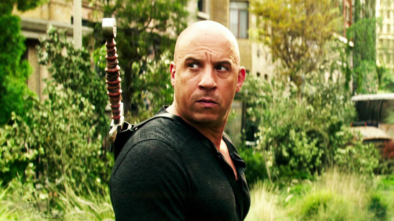 Vin Diesel as Kaulder turns to look behind him while walking through a city street overgrown with trees and grass in The Last Witch Hunter