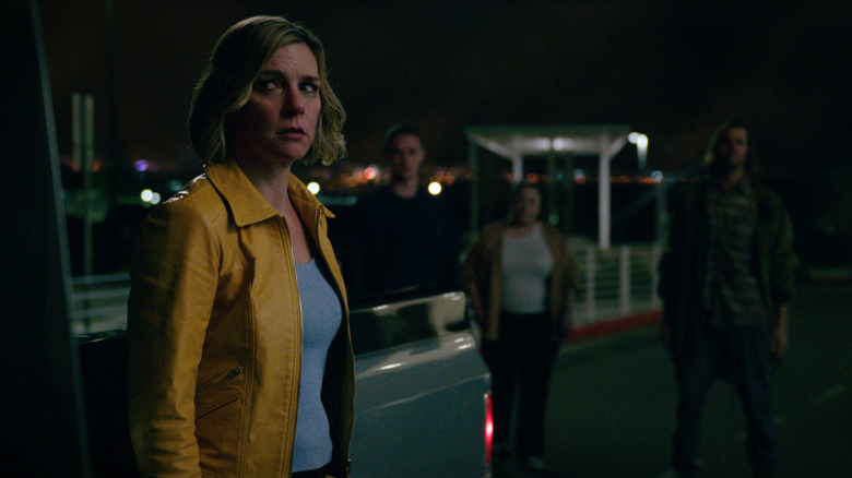 Rhea Seehorn's Carol Sturka standing beside a car with ominous figures on the background on Pluribus