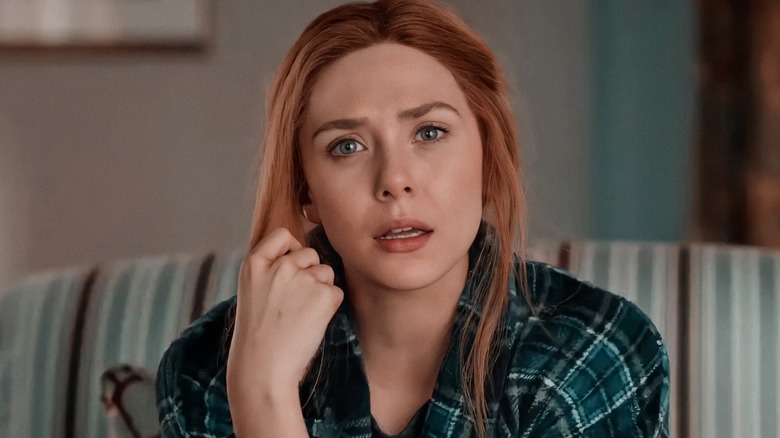Elizabeth Olsen as Wanda Maximoff sitting on a coach with a confused expression on her face in WandaVision
