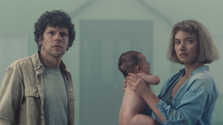 Gemma holds baby while standing in street with Tom in Vivarium